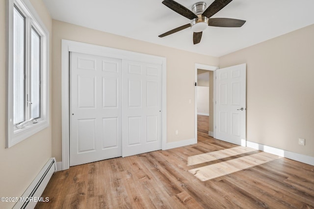 unfurnished bedroom with ceiling fan, a baseboard radiator, light wood-type flooring, a closet, and multiple windows