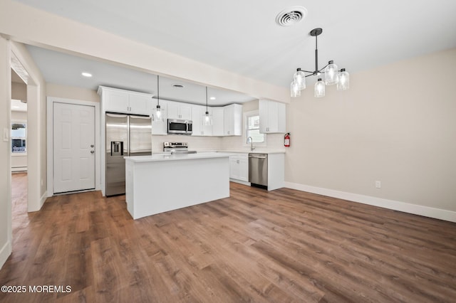 kitchen featuring white cabinets, hanging light fixtures, appliances with stainless steel finishes, and a kitchen island