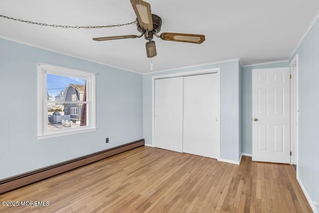 unfurnished bedroom featuring baseboard heating, a closet, light wood-type flooring, ceiling fan, and crown molding