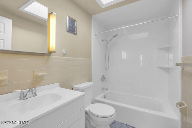 full bathroom featuring toilet, vanity, tile walls, a skylight, and bathing tub / shower combination