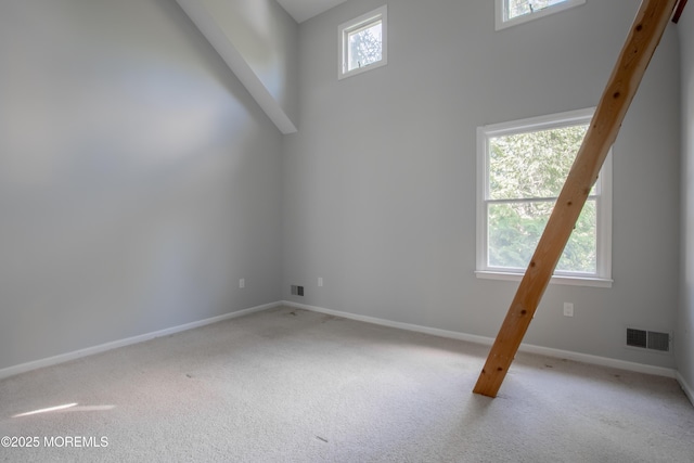 carpeted empty room with a towering ceiling, visible vents, and baseboards