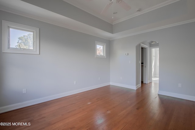 empty room with arched walkways, a healthy amount of sunlight, baseboards, and wood finished floors