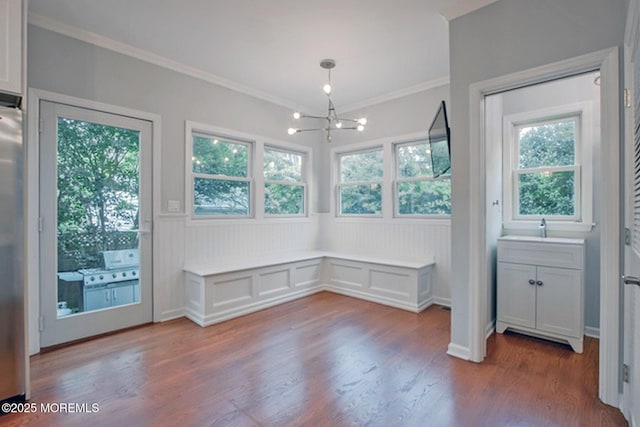 unfurnished dining area featuring dark wood-style floors, a chandelier, wainscoting, and ornamental molding