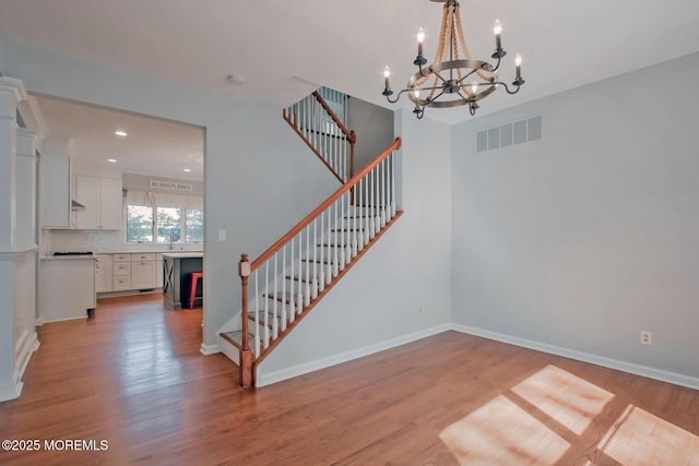 staircase with a chandelier, visible vents, baseboards, and wood finished floors