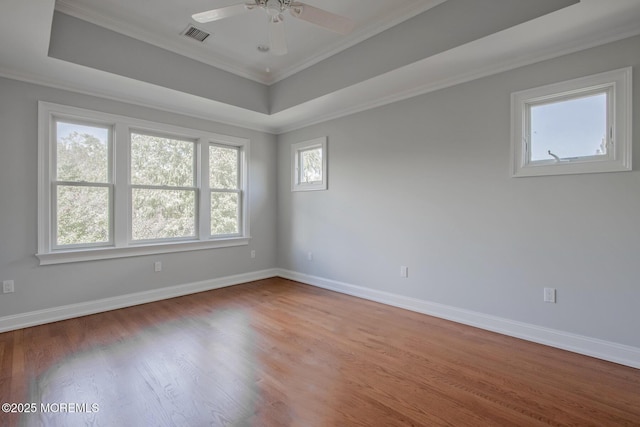 empty room with a raised ceiling, crown molding, baseboards, and wood finished floors