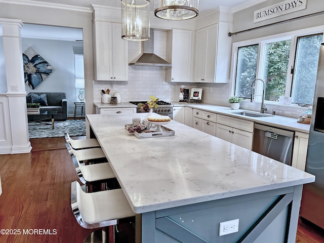 kitchen featuring light stone counters, stainless steel appliances, a sink, ornamental molding, and wall chimney range hood