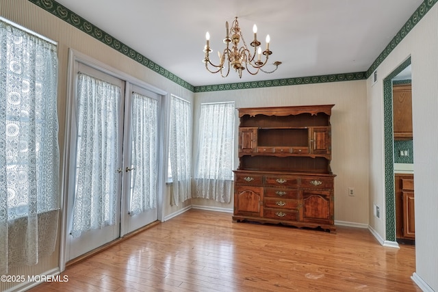 unfurnished dining area featuring a chandelier, light wood-type flooring, and french doors