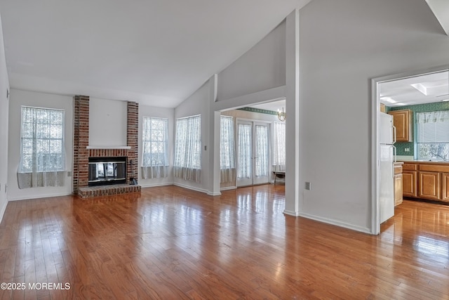 unfurnished living room with high vaulted ceiling, a fireplace, and light hardwood / wood-style floors