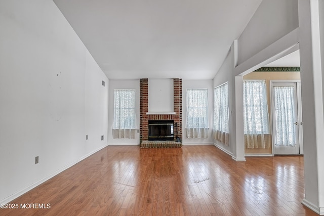 unfurnished living room with lofted ceiling, a brick fireplace, and light wood-type flooring