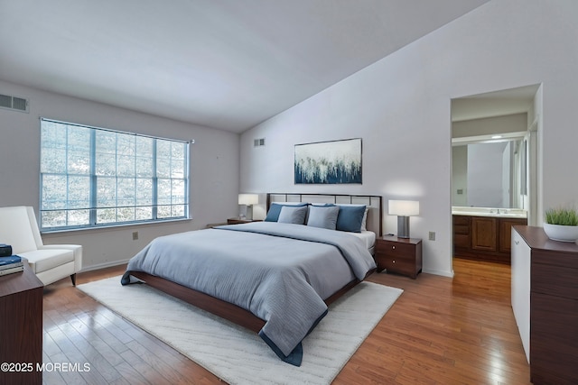 bedroom with ensuite bath, wood-type flooring, sink, and lofted ceiling