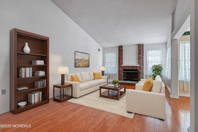 living room featuring vaulted ceiling, a fireplace, and light hardwood / wood-style floors