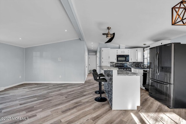 kitchen featuring white cabinets, black appliances, a center island, decorative backsplash, and light stone counters