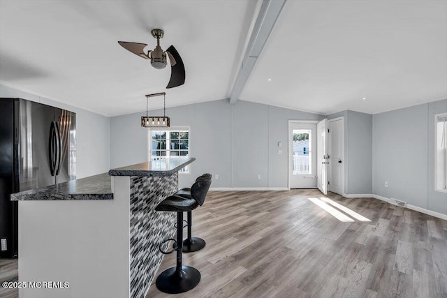 kitchen with light hardwood / wood-style floors, a kitchen breakfast bar, decorative light fixtures, vaulted ceiling with beams, and black fridge