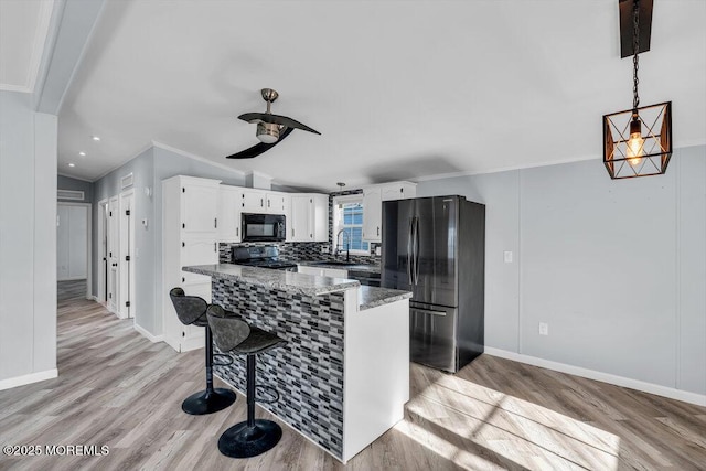 kitchen featuring light hardwood / wood-style flooring, ceiling fan, white cabinetry, dark stone countertops, and black appliances