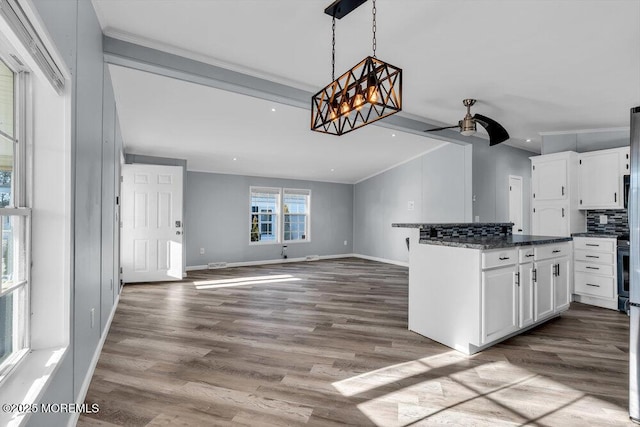 kitchen featuring wood-type flooring, decorative light fixtures, backsplash, white cabinets, and dark stone counters