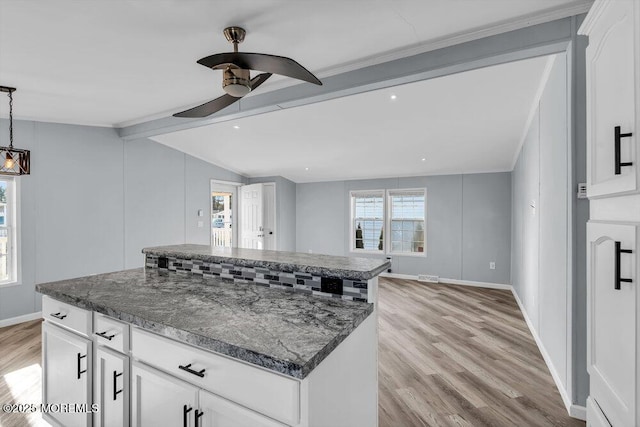 kitchen with white cabinets, a center island, dark stone countertops, vaulted ceiling with beams, and ceiling fan