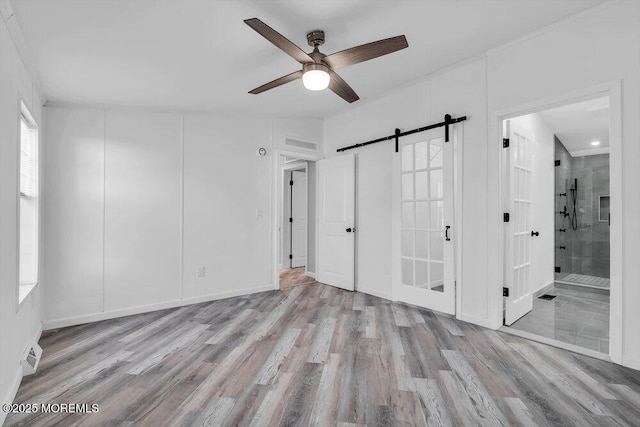 empty room with light wood-type flooring, ceiling fan, and a barn door