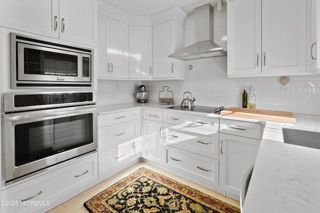 kitchen with appliances with stainless steel finishes, wall chimney exhaust hood, backsplash, white cabinetry, and light stone countertops