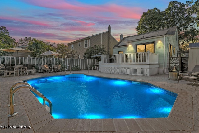 pool at dusk with a wooden deck, an outdoor structure, and a patio