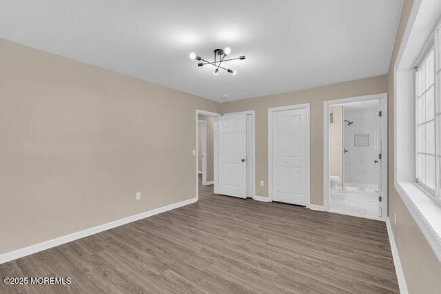 unfurnished bedroom featuring ensuite bath, a notable chandelier, and hardwood / wood-style floors