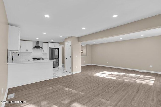 kitchen with wall chimney exhaust hood, white cabinetry, stainless steel refrigerator, kitchen peninsula, and light wood-type flooring