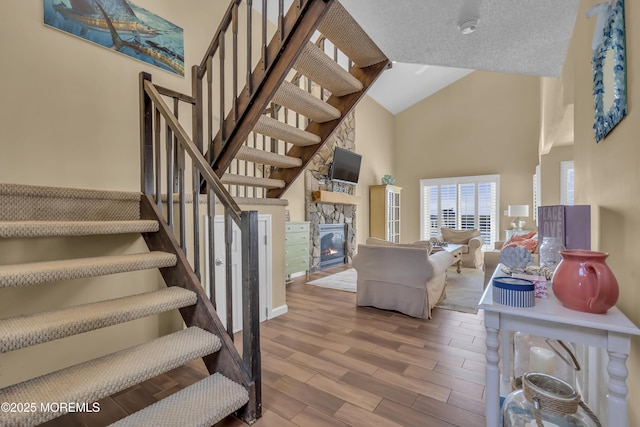 staircase with a stone fireplace and high vaulted ceiling