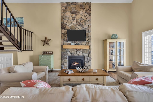 living room with a stone fireplace, light hardwood / wood-style flooring, and a high ceiling