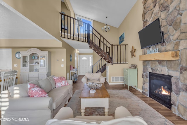 living room featuring a stone fireplace, a towering ceiling, hardwood / wood-style floors, and a notable chandelier