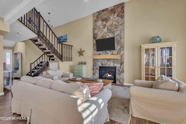 living room with wood-type flooring, a stone fireplace, and a towering ceiling