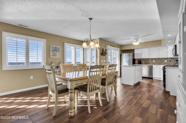 dining room with ceiling fan with notable chandelier, dark wood-type flooring, and a textured ceiling