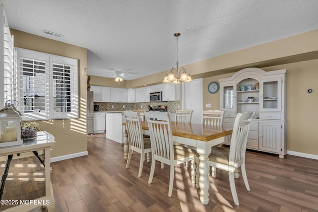 dining room featuring ceiling fan with notable chandelier, dark wood-type flooring, and a textured ceiling