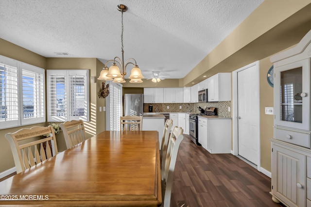 dining room with ceiling fan with notable chandelier, dark hardwood / wood-style floors, and a textured ceiling