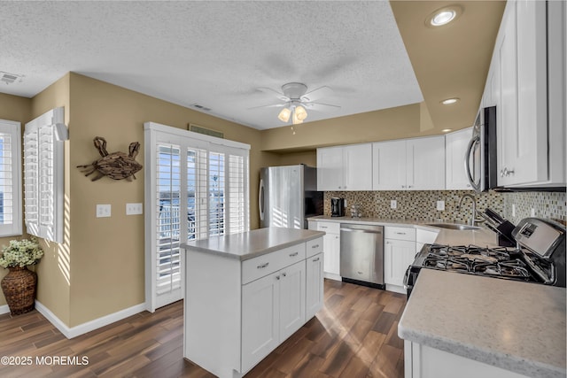 kitchen with appliances with stainless steel finishes, white cabinetry, sink, a center island, and dark wood-type flooring