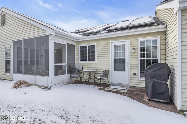 snow covered rear of property with a sunroom and solar panels