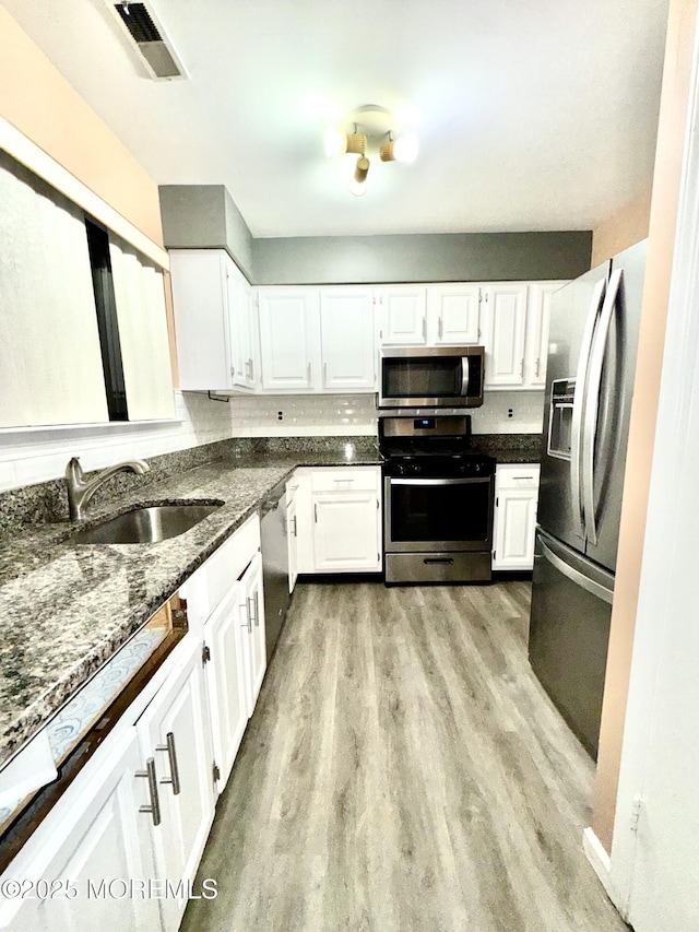 kitchen with sink, light wood-type flooring, stainless steel appliances, white cabinets, and dark stone counters