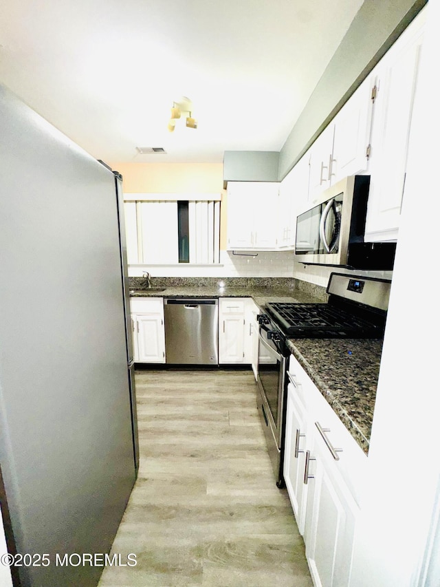 kitchen with light wood-type flooring, appliances with stainless steel finishes, dark stone counters, and white cabinetry