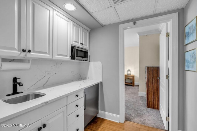 kitchen with white cabinetry, stainless steel microwave, baseboards, backsplash, and a sink