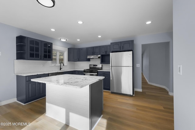 kitchen featuring appliances with stainless steel finishes, a center island, wood-type flooring, light stone countertops, and sink