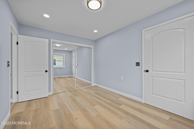 unfurnished bedroom with baseboard heating, a closet, and light hardwood / wood-style flooring