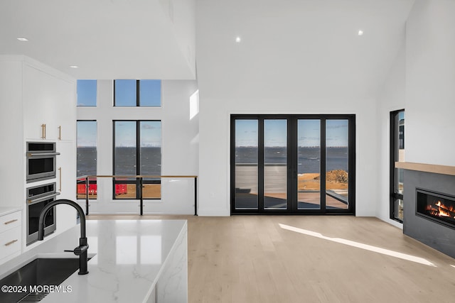 living room featuring sink, a towering ceiling, a water view, and a healthy amount of sunlight