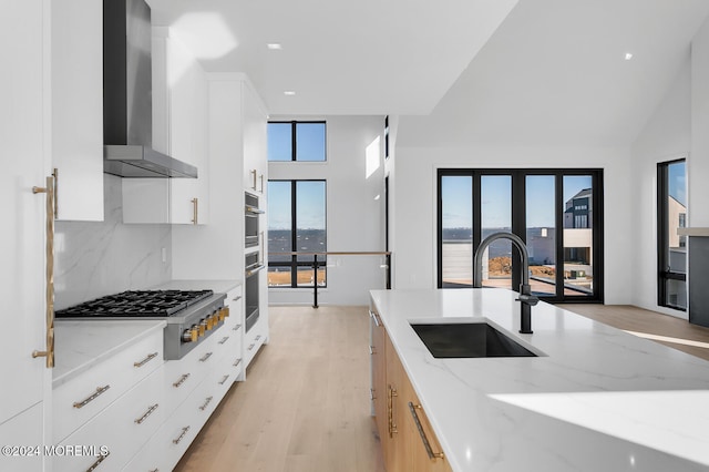 kitchen with light stone countertops, wall chimney range hood, white cabinets, sink, and stainless steel appliances