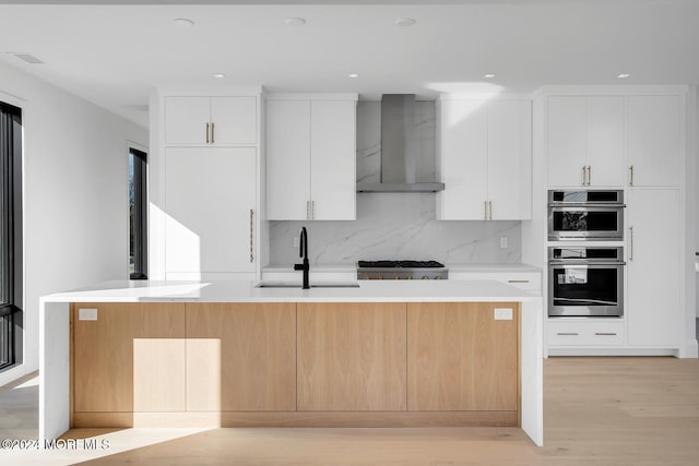 kitchen featuring sink, wall chimney range hood, white cabinets, and a center island with sink