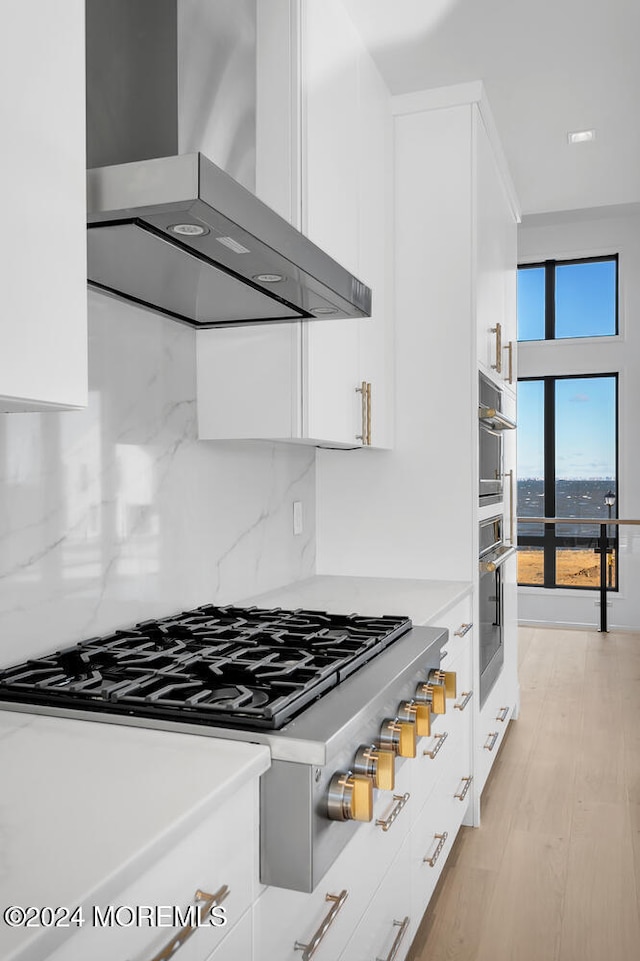 kitchen with wall chimney exhaust hood, white cabinets, tasteful backsplash, and light wood-type flooring