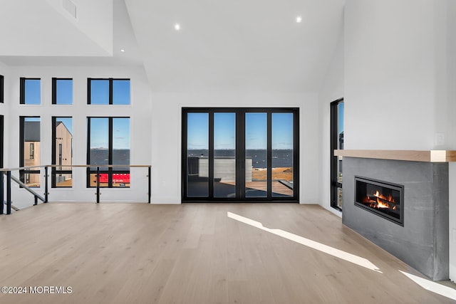 unfurnished living room with light wood-type flooring and a towering ceiling