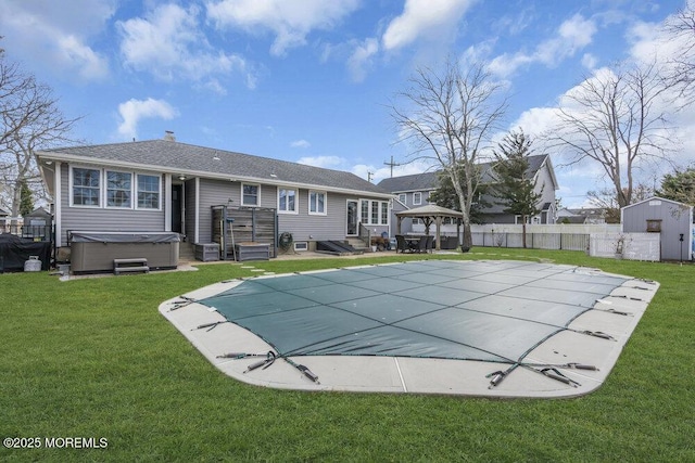 back of house featuring a hot tub, a gazebo, a storage unit, and a lawn