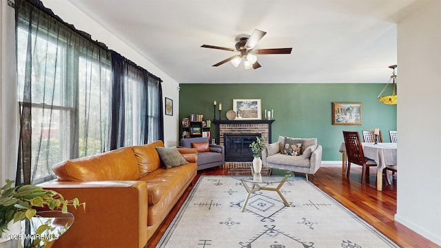 living room featuring a brick fireplace, wood-type flooring, ceiling fan, and plenty of natural light