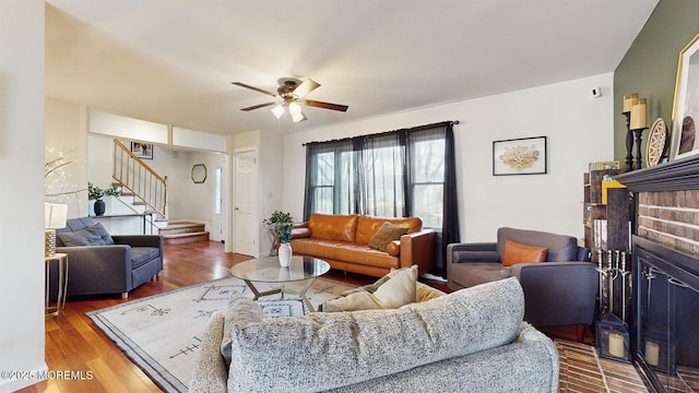 living room featuring ceiling fan, wood-type flooring, and a brick fireplace