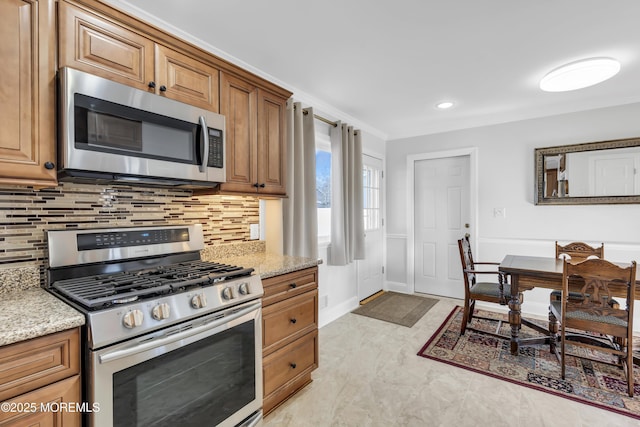 kitchen with light stone countertops, appliances with stainless steel finishes, ornamental molding, and tasteful backsplash