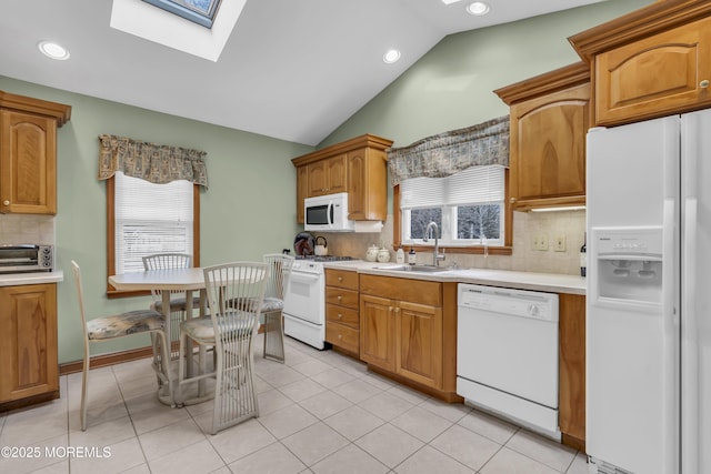 kitchen featuring white appliances, tasteful backsplash, light tile patterned floors, vaulted ceiling with skylight, and sink