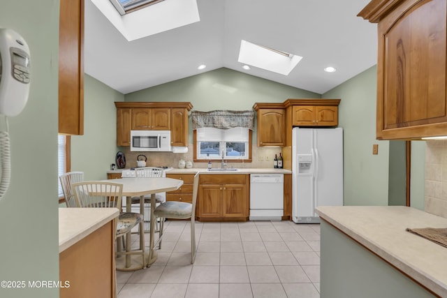 kitchen featuring vaulted ceiling with skylight, white appliances, tasteful backsplash, sink, and light tile patterned floors